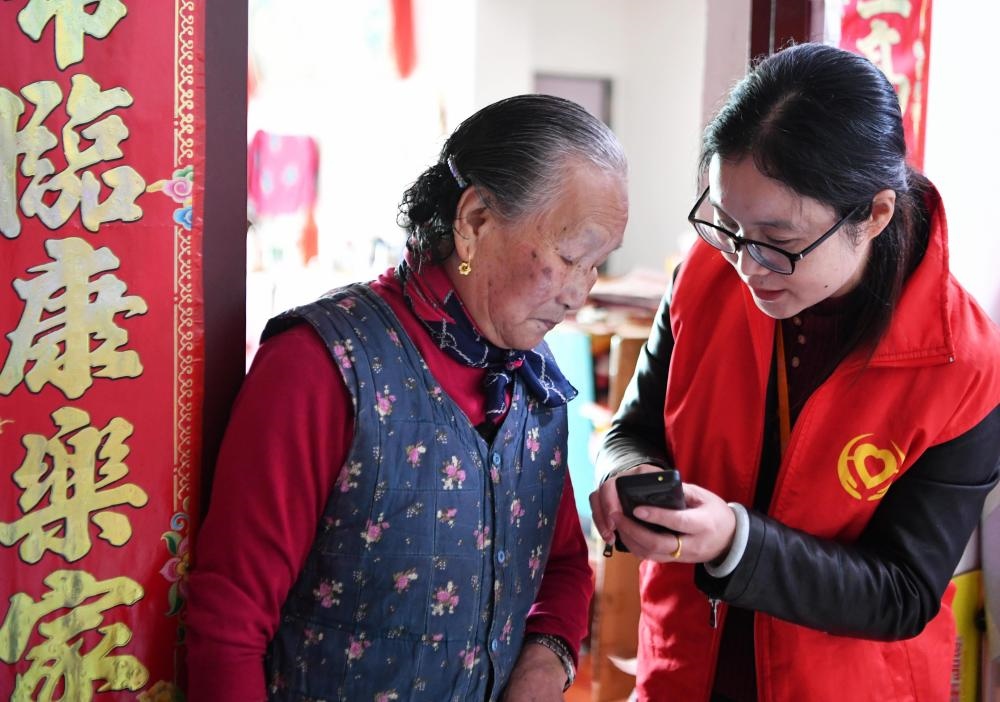 在福州市長樂區(qū)航城街道籌岐村，智慧養(yǎng)老平臺派駐社區(qū)的助老員（右）在為老人陳鳳英（左）講解養(yǎng)老定制手機的用法（2021年11月26日攝）。新華社記者 魏培全 攝