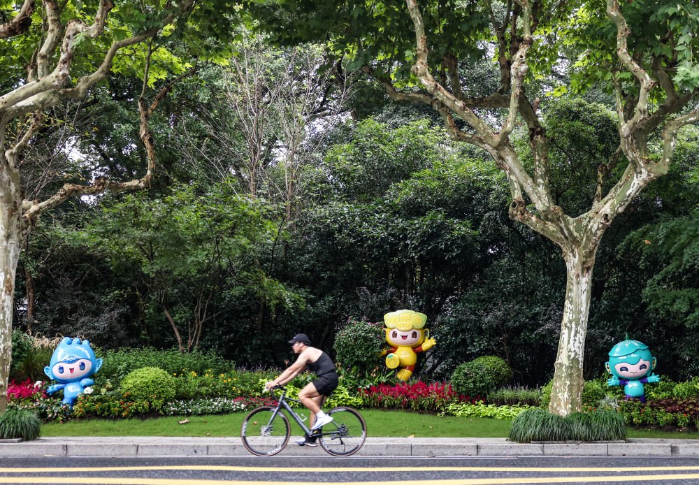 市民在杭州市南山路上一處亞運會主題吉祥物雕塑前騎自行車。