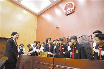 圖③：同學(xué)們穿法袍、敲法槌，爭(zhēng)做“小法官”。