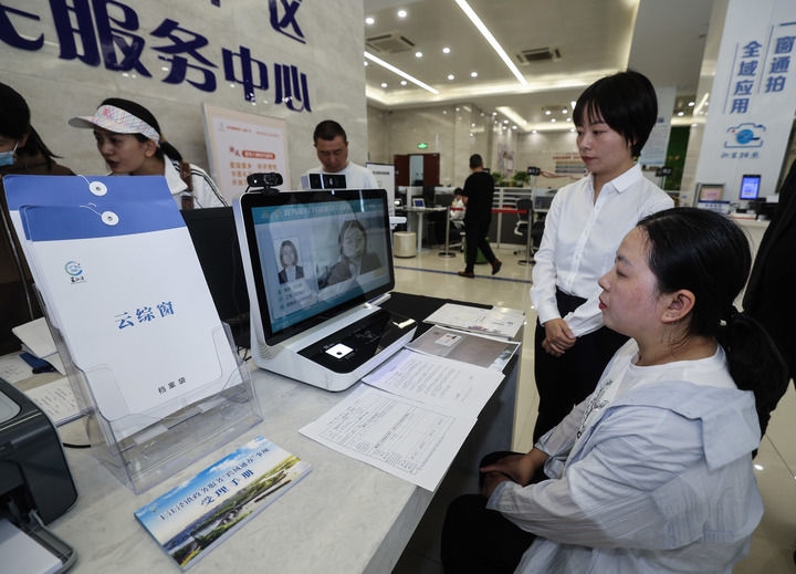 在浙江省嘉興市秀洲區(qū)王江涇鎮(zhèn)便民服務(wù)中心的“跨域通辦·云綜窗”窗口，辦理開業(yè)登記的個體工商戶（右一）通過該系統(tǒng)與江蘇省蘇州市吳江區(qū)盛澤鎮(zhèn)行政審批局工作人員視頻連線，進行身份讀取及材料線上審核（2024年5月9日攝）。新華社記者 徐昱 攝