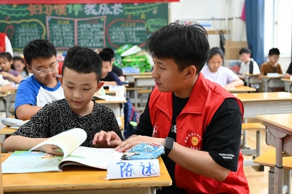 鄭州市二七區(qū)暑托班的志愿者輔導(dǎo)孩子寫作業(yè)。人民網(wǎng)記者王玉興攝